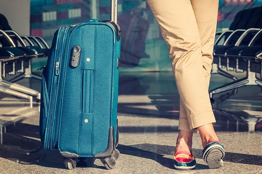 Legs of young woman close-up and blue baggage in airport